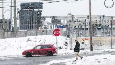  ??  ?? A pedestrian crosses Quesnel Street in Victoria as snow begins to fall near a B.C. Hydro substation on Thursday.