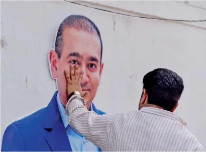  ?? AFP ?? A supporter of the Congress Party keeps his hand on the face of a cutout of jeweller Nirav Modi during a protest in New Delhi. —