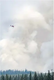  ?? DARRYL DYCK /THE CANADIAN PRESS ?? A helicopter used to fight a smaller fire nearby flies past a large plume of smoke rising from a wildfire near Fraser Lake, B.C., on Wednesday.