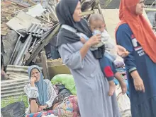  ?? ?? Villagers wait for aid supplies near quake-hit houses.