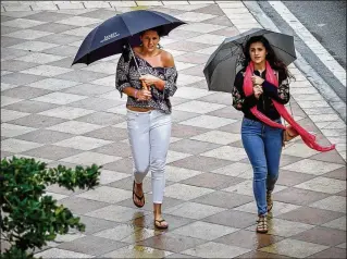  ?? RICHARD GRAULICH / THE PALM BEACH POST ?? WEST PALM BEACH: Two women walk around the Harriet Himmel Theatre in CityPlace during a light rain on Tuesday. Forecaster­s expect the low in West Palm to be 38 on Thursday.