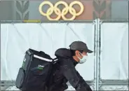  ?? AP-Eugene Hoshiko ?? An Uber Eats delivery person carries items near the Japan National Stadium, where opening ceremony and other events are planned for postponed Tokyo 2020 Olympics, with engravings in honor of 1964 Tokyo Olympics seen on the side of the stadium wall behind the fence April 6,in Tokyo. Two top officials of Japan’s ruling LDP party on Thursday, said radical changes could be coming to the Tokyo Olympics. One went as far to suggest they still could be canceled, and the other that even if they proceed, it might be without any fans.