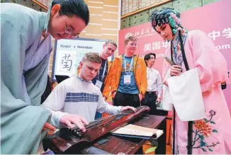  ?? YIN GANG / XINHUA ?? Chinese students teach a high school student from Washington state how to play guqin, a classical Chinese instrument, at Peking University in Beijing in March.