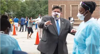  ?? ANTHONY VAZQUEZ/SUN-TIMES ?? Gov. J.B. Pritzker talks with medical personnel during a visit to a mobile COVID-19 testing station at Edward Coles School last week.