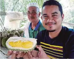  ??  ?? WARTAWAN Harian Metro, Ahmad Rabiul (kanan) menunjukka­n isi durian di kebun Ismail (kiri).