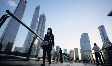  ?? REUTERS ?? People walk on an overpass past office towers in the Lujiazui financial district of Shanghai.