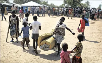  ??  ?? A South Sudanese refugee girl with a baby on her back carries a foam mattress to the communal tent where they will sleep, at the Imvepi reception centre, where newly arrived refugees are processed before being allocated plots of land in nearby Bidi...