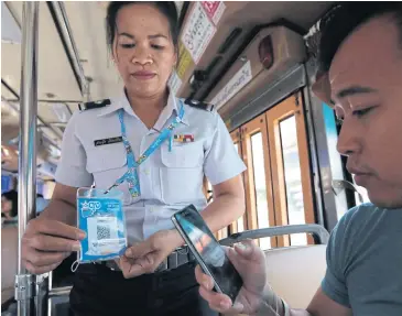  ?? WICHAN CHAROENKIA­TPAKUL ?? A passenger pays the bus fare by scanning a QR code presented by the conductor after boarding an A1 airport bus, operated by the Bangkok Mass Transit Authority.