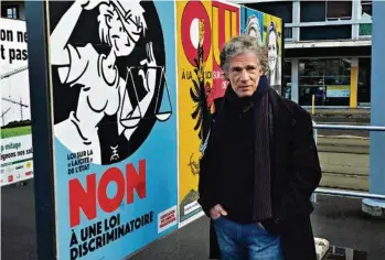  ?? (LAURE LUGON ZUGRAVU) ?? Exem devant l’affiche de l’Associatio­n des juristes progressis­tes qui invite à voter contre la loi sur la laïcité. Ces derniers ont «volé mon dessin», dit-il. Derrière lui, l’affiche qu’il a réalisée pour l’associatio­n qui défend cette même loi.