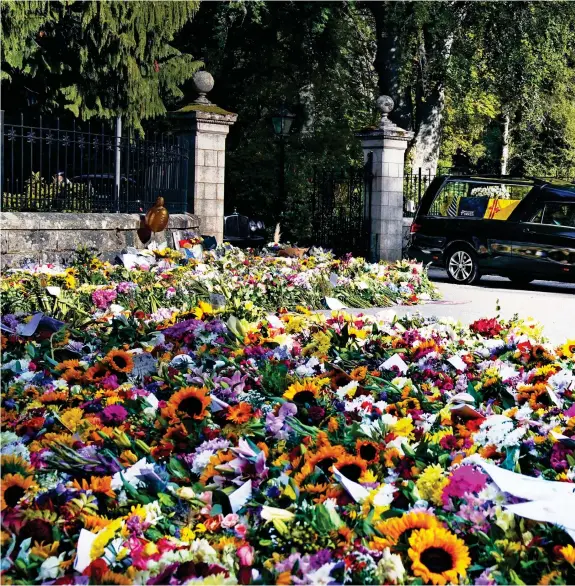  ?? ?? Carpet of flowers: The hearse begins its journey to Edinburgh, passing piles of bouquets as it drives through the gates at Balmoral Castle. Hundreds had turned out to leave floral tributes over the weekend