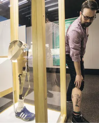  ??  ?? Royal B.C. Museum design worker Steve Lewis shows his tattoo of Terry Fox’s prosthetic leg next to a real one on display at the Terry Fox exhibit opening Wednesday.