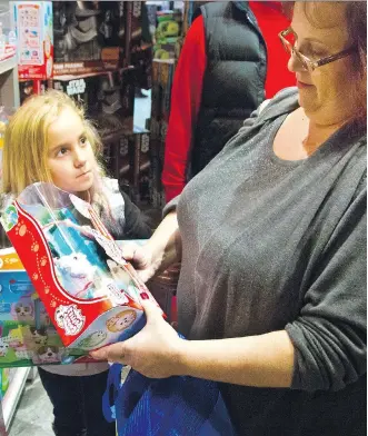  ?? BEBETO MATTHEWS/ THE ASSOCIATED PRESS FILES ?? A woman checks out a Chubby Puppies toy for her daughter at a Toys “R” Us. With some holiday toys already in stores, shoppers may want to start planning their strategy.
