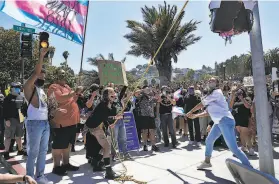  ?? Carlos Avila Gonzalez / The Chronicle ?? Raymond Quitugua, left, of Sacramento carries the Trans Flag, and Elisha Carlisle, right, of Oakland takes a swing at a police car piñata during the S.F. march.