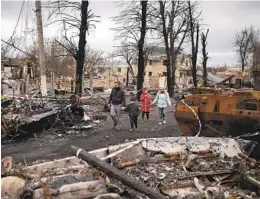  ?? FELIPE DANA AP ?? A family walks amid destroyed Russian tanks in Bucha, outside Kyiv, Ukraine, on Wednesday. Russian troops are believed to have killed more than 300 civilians.