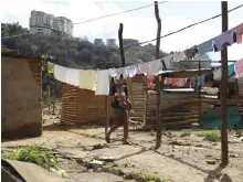  ?? ?? A woman walks across hanged clothes on a vacant lot where families are settling since they cannot afford to pay rent anymore (Reuters)