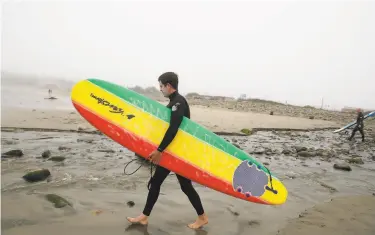  ?? Lea Suzuki / The Chronicle ?? Andrew Knell carries his surfboard on Pacifica State Beach as he prepares to go surfing, which is allowed.