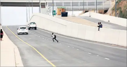  ?? PICTURES: NQOBILE MBONAMBI ?? ACCIDENT WAITING TO HAPPEN?: In the shadow of a safe pedestrian bridge, young children hop over the concrete walls dividing lanes on the Dumisani Makhaye Freeway, taking their own short cut home from school over the new road.