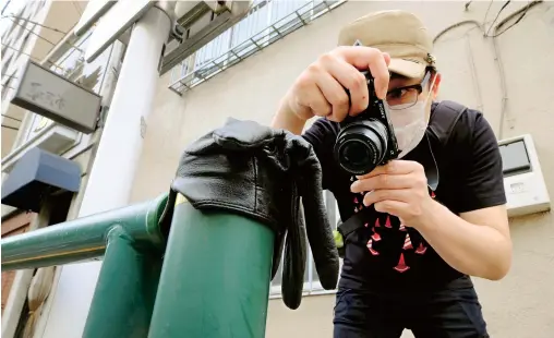  ??  ?? Japanese photograph­er Koji Ishii takes pictures of a lost glove on a pole beside the road in Tokyo. — AFP