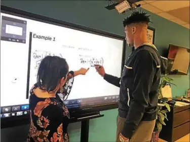  ??  ?? The Lincoln Center Leadership Academy’s Lauryn Grau helps a student work on a math problem on the newly purchased Aquos board.