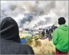  ?? PHILIPPE HUGUEN ?? Migrants look at smoke rising over makeshift shelters on fire at the ‘Jungle’ migrant camp yesterday.