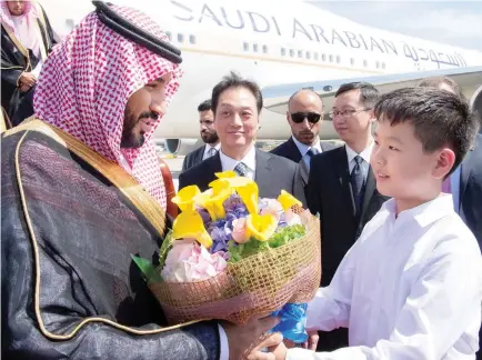  ??  ?? Deputy Crown Prince Mohammed bin Salman being welcomed with a bouquet by a schoolboy upon his arrival in Beijing on Monday. (Reuters)