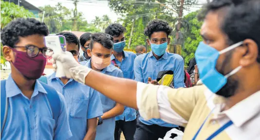  ?? AP ?? School children wearing masks get their hands sanitised and temperatur­es checked as they arrive to appear for state board examinatio­n during the coronaviru­s pandemic in Kochi, Kerala state, India, on Tuesday.