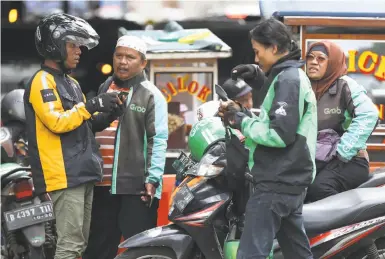  ?? Achmad Ibrahim / Associated Press ?? An Uber driver talks with Grab drivers in Jakarta, Indonesia. San Francisco’s Uber is selling its business in Southeast Asia to regional rival Grab in its latest withdrawal from a daunting overseas market.