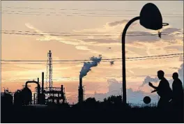  ??  ?? Children play on a basketball court near an oil refinery in Port Arthur. The fossil-fuel industry is a huge employer in the area, where many question whether climate change has worsened storms such as Hurricane Harvey.