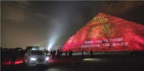  ?? — AFP photo ?? People take pictures in front of the Great pyramid of Kheops where a laser projection writes ‘Stay at home, stay safe. Thanks to those keeping us safe’ amid the spread of the Covid-19 infection, caused by the novel coronaviru­s.