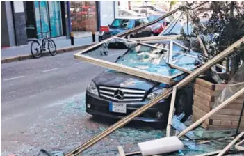  ??  ?? O Un vehículo aplastado por ventanas caídas de los edificios en la calle Hamra, a 1,8 km del sitio de las explosione­s.