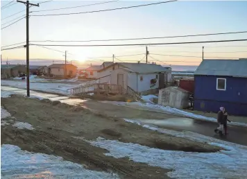  ?? TREVOR HUGHES/USA TODAY ?? The sun sits low over Shishmaref, Alaska, as two residents walk home from an evening trip to the store.