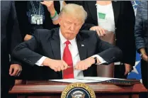  ??  ?? President Donald Trump takes the cap off a pen before signing an executive order to build a wall on the Mexican border.
