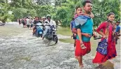  ?? PTI ?? Commuters wade through a flooded road after heavy rains, in Kamrup district on Sunday. —