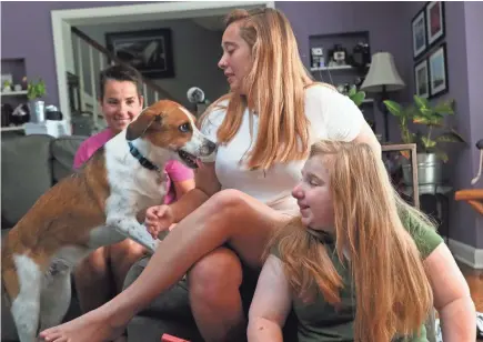  ?? MICHAEL SEARS/MILWAUKEE JOURNAL SENTINEL ?? Terri Hart-Ellis (from left) and daughters Catriona Ellis, 19, and Addie Ellis, 15, play with Mykonos, the family's rescue dog. Mykonos is very protective of Addie, who has Rubinstein-Taybi syndrome.