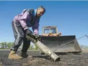  ?? ANDRII MARIENKO/AP ?? A farmer pulls a piece of a Russian missile Saturday from his field in Izium in Ukraine’s Kharkiv region.