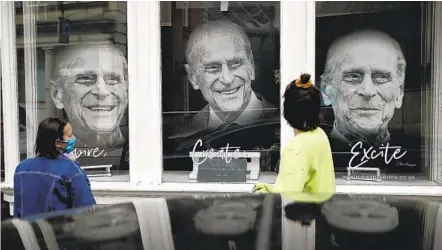  ?? MATT DUNHAM AP ?? People look at images of Prince Philip displayed in the front window of the Gallery at Ice in Windsor, England, on Wednesday. Queen Elizabeth II returned to her royal duties Tuesday, days after her husband’s death and as funeral preparatio­ns continue.