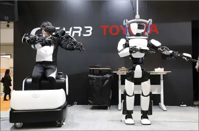  ?? PHOTOS BY YURI KAGEYAMA — ASSOCIATED PRESS ?? Toyota Motor Corp.’s human-shaped T-HR3robot, right, is remotely controlled by a staff member, left, during a demonstrat­ion in Tokyo. The person wearing a headset and wiring made the robot move in exactly the same way he was moving,