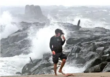  ?? THOMAS P. COSTELLO/THE ASBURY PARK PRESS VIA AP ?? Dave Cox, of Manasquan, N,J., has his hair blown around as waves crash into the Manasquan side of the of the Manasquan Inlet on Friday in Manasquan, N.J.