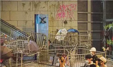  ?? AFP PIC ?? Protesters walking past barricades and a wall with remnants of thrown eggs and graffiti sprayed by protesters outside the police headquarte­rs in Hong Kong yesterday.