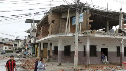  ?? (Guillermo Granja/Reuters) ?? PEOPLE WALK by damaged buildings yesterday after an earthquake struck off Ecuador’s Pacific coast, at Tarqui neighborho­od in Manta.