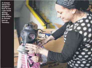  ?? ABIR SULTAN, EPA ?? A woman shows her daughter how to use a gas mask during distributi­on of kits in Jerusalem on Tuesday.