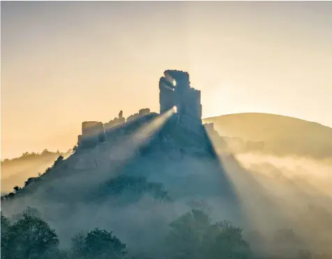  ??  ?? Early morning mist lifts over Corfe Castle in Dorset yesterday, making way for the warm sunshine as the country embraced the early Bank Holiday heatwave