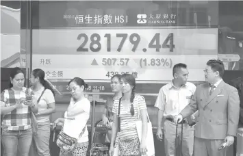  ?? ASSOCIATED PRESS ?? People stand in front of an electronic board showing the Hong Kong share index outside a bank in Hong Kong, Monday, Aug. 27, 2018. Asian stocks are rising as a dovish speech by U.S. Federal Reserve Chairman Jerome Powell and all-time highs on Wall Street gave markets a breather from trade tensions.