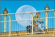  ?? AP/J. DAVID AKE ?? The moon looms large in the background as a cyclist rides across the Francis Scott Key Bridge toward the Georgetown neighborho­od Wednesday morning in Washington, D.C.