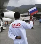  ?? FOTO: MATIAS
DELACROIX/TT-AP-ARKIV ?? En vårdarbeta­re håller upp den ryska flaggan medan Sputnik V lastas av ett flygplan i Venezuela – som är ett av de länder som tar emot Rysslands vaccin.