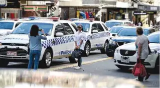  ??  ?? MELBOURNE: Tourists take photos between police cars after a car ploughed into pedestrian­s in the center of Melbourne yesterday. — AFP