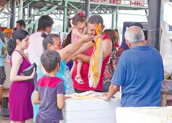  ??  ?? Una vendedora de pescado exhibe un dorado a un cliente. Cientos de personas aprovechar­on el ultimo día para comprar especies frescas. pues desde hoy rige la veda pesquera.