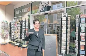  ?? FOTO: UWE PLIEN ?? Buchhändle­rin Petra Neumann mit einem Brownie. „Komm rein und fühl dich wohl“, steht auf der Tafel vor der Ladentür.