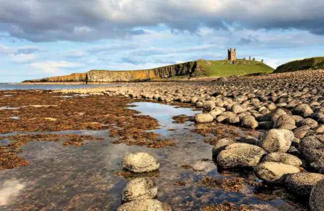  ??  ?? Dunstanbur­gh Castle, a popular subject for artists, rises in the distance beyond the rock pools among Greymare Rocks, at the southern end of Embleton Bay.