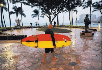  ?? John Locher ?? The Associated Press A surfer walks Saturday along Honolulu’s Waikiki Beach amid gray skies and a light rain from Tropical Storm Lane.